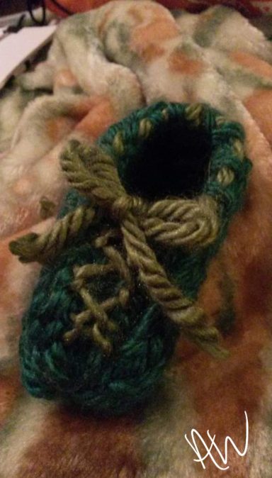 A small, green hand-knit shoe with a bow and decorative stitches.