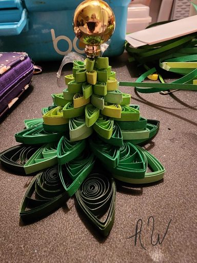 A decorative green paper tree with a golden top, featuring layered leaf shapes.