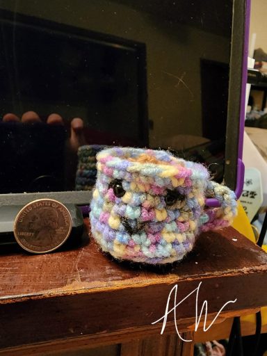 Colorful crocheted mug with a smiley face, next to a coin for scale.