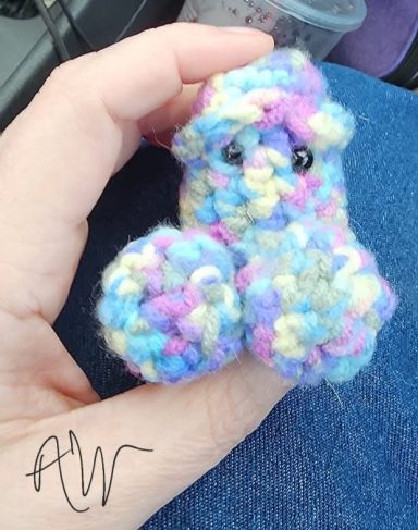 A small, colorful, knitted creature with large eyes, held in a hand.